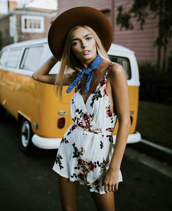 Chica rubia delgada vistiendo jumper blanco con flores y un sombrero café mientras pone la mano derecha en la cabeza