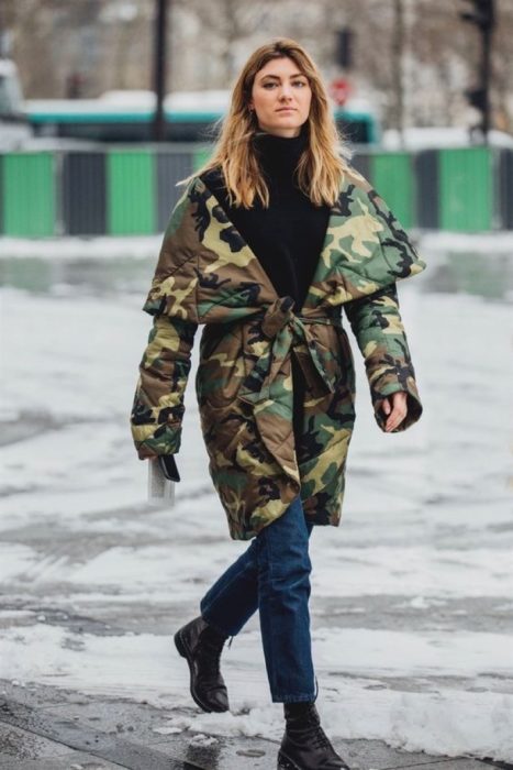 Chica caminando con jeans, blusa negra, botas y chaqueta verde militar