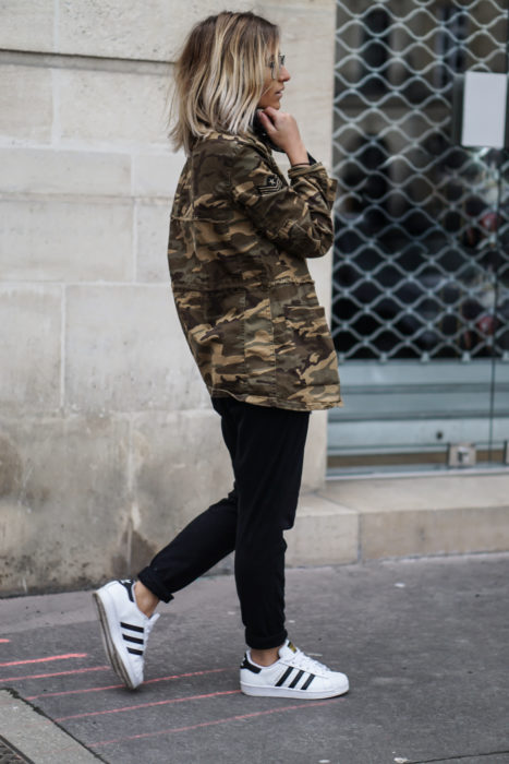 Chica caminando con jeans, blusa negra, botas y chaqueta verde militar