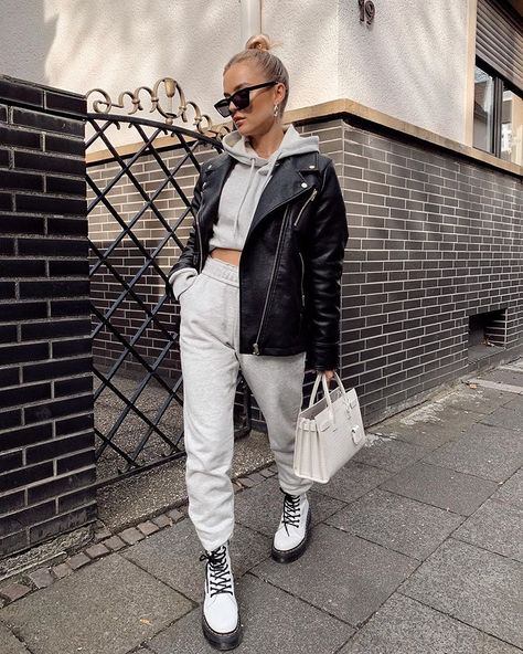 Chica usando joggers, sudadera y chaqueta de cuero con botas Dr. Martens blancas mientras camina por la calle