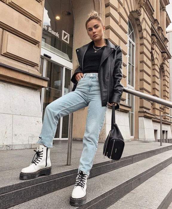 Chica usando jeans, chaqueta de cuero, blusa negra y botas Dr. Martens blancas con cintas negras