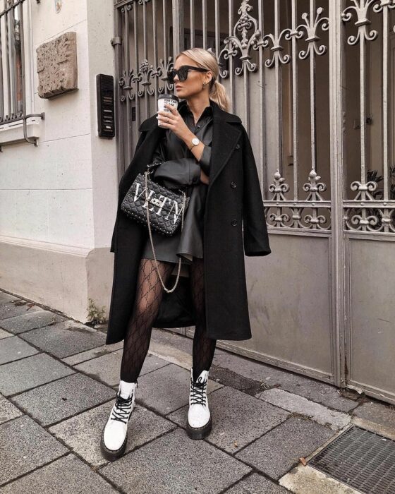 Chica usando un outfit negro con botas Dr. Martens blancas mientras toma café y posa para una foto
