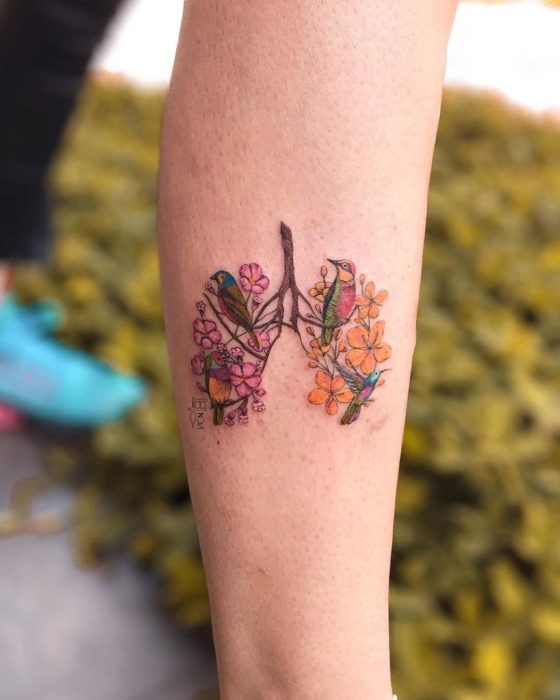 Tatuaje de flores en el antebrazo donde se ve la silueta de unos pulmones decorados con varias plantas