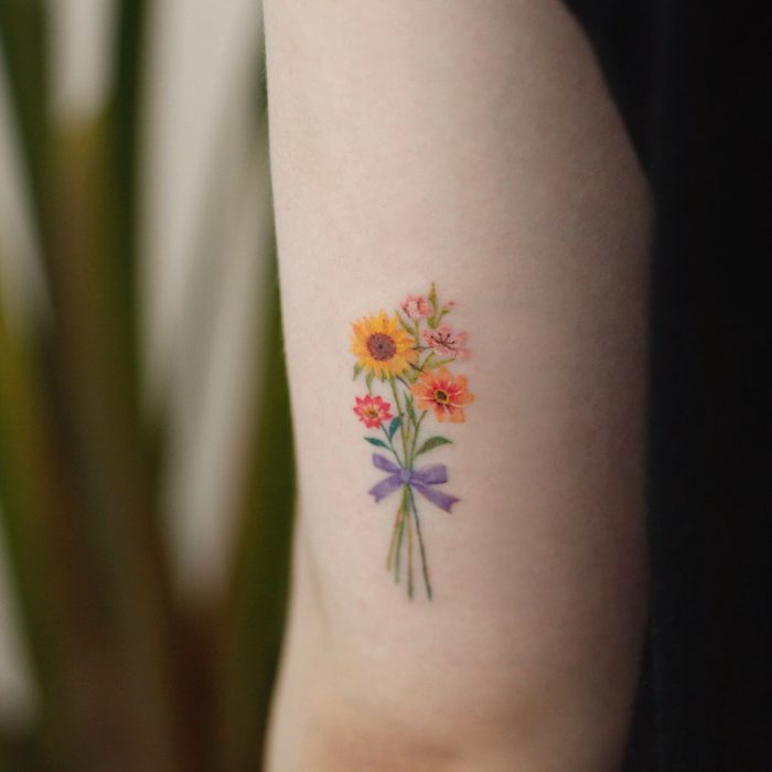 Tatuaje de flores en el brazo, un ramo de flores atado con un listón morado