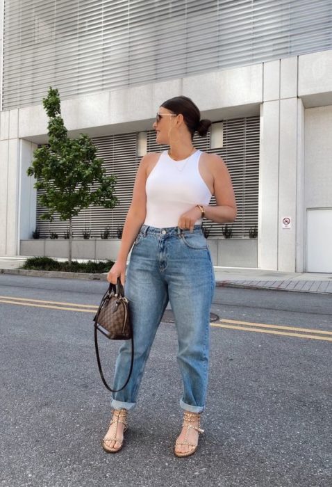 chica de cabello castaño con playera sin mangas blanca, bolso café de piel y jeans slouchy