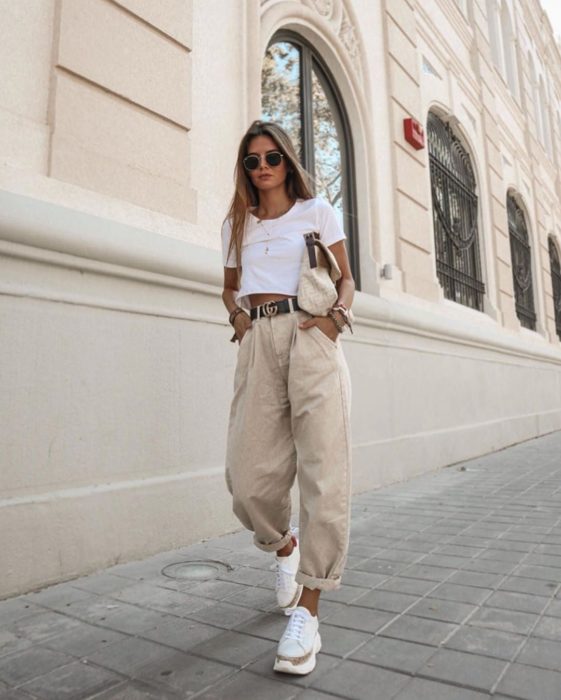 chica rubia con playera blanca de manga corta, cinturón negro, slouchy jeans de pana, lentes de sol y tenis blancos