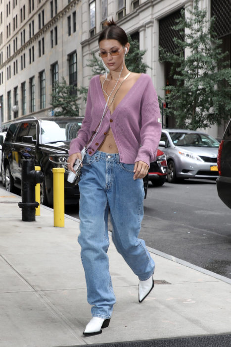modelo Bella Hadid usando slouchy jeans, cárdigan lila y botas blancas de piel
