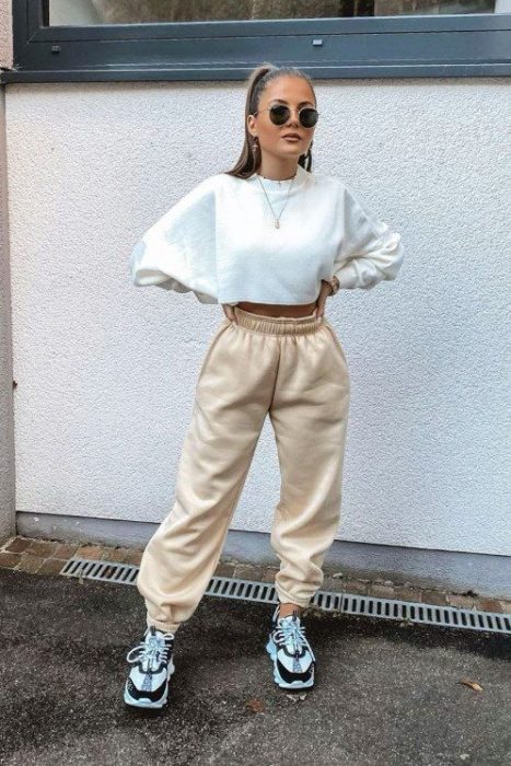 chica de cabello castaño con sudadera blanca, pants beige y tenis deportivos blancos y negros