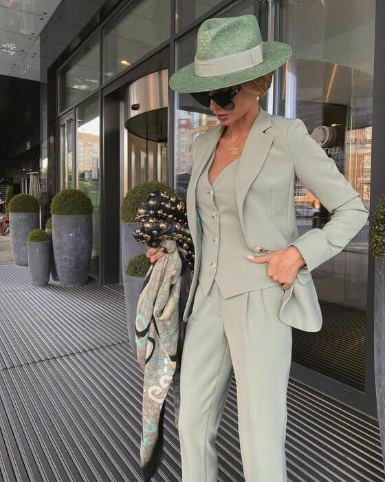 Victoria Fox usando traje sastre con pantalón, chaleco y saco verde, y sombrero a juego