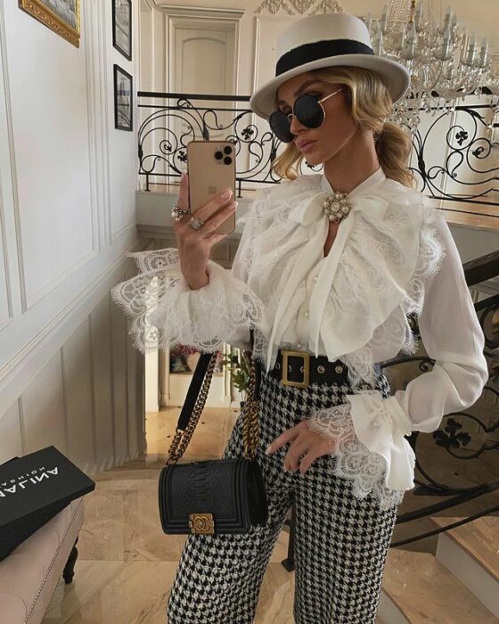 Victoria Fox usando pantalones de cuadros en blanco y negro, con blusa blanca, sombrero y bolsa negra