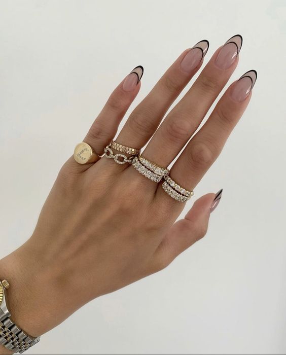 Mano delgada con anillos en cada dedo y uñas largas en forma de almendra con puntas decoradas con líneas negras
