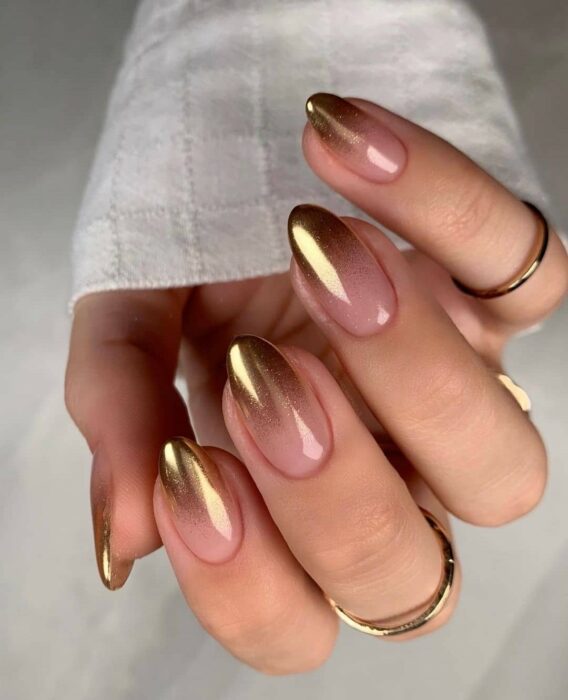 Uñas en forma ovalada con detalles dorados y un acabado natural