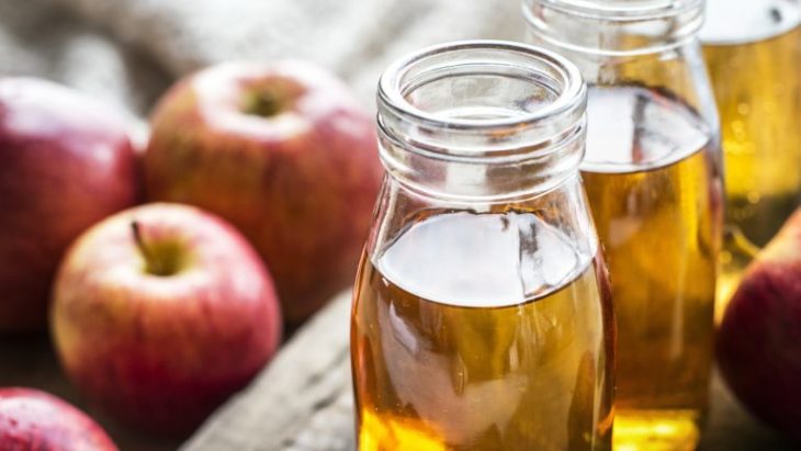 Frasco relleno de vinagre de manzana junto a unas manzanas frescas