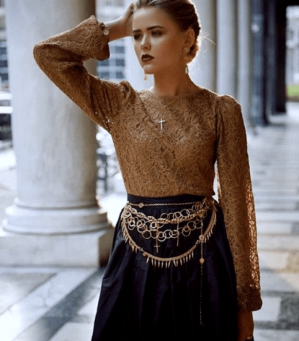 chica de cabello claro usando una blusa amarilla con mangas holgadas, falda negra con cinturón metálico dorado