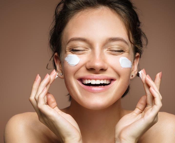 Chica aplicando crema sobre sus mejillas