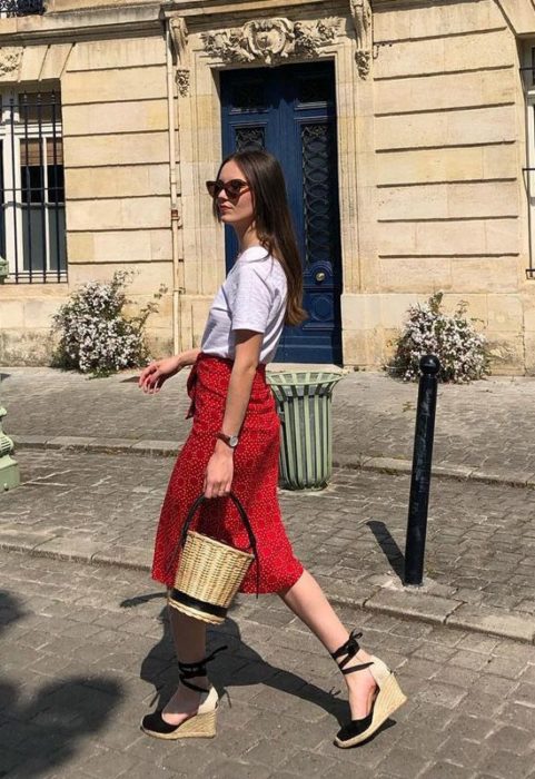 Chica usando falda roja, camiseta blanca, alpargatas negras y bucket bag de mimbre