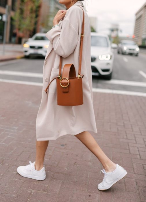 Chica usando tenis blancos, un blazer largo y bucket bag color camel