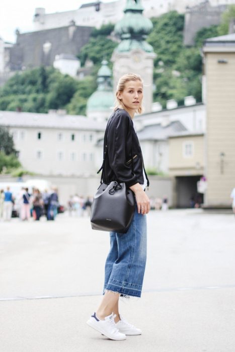 Chica usando tenis blancos, mom jeans, camisa negra y bucket bag negra