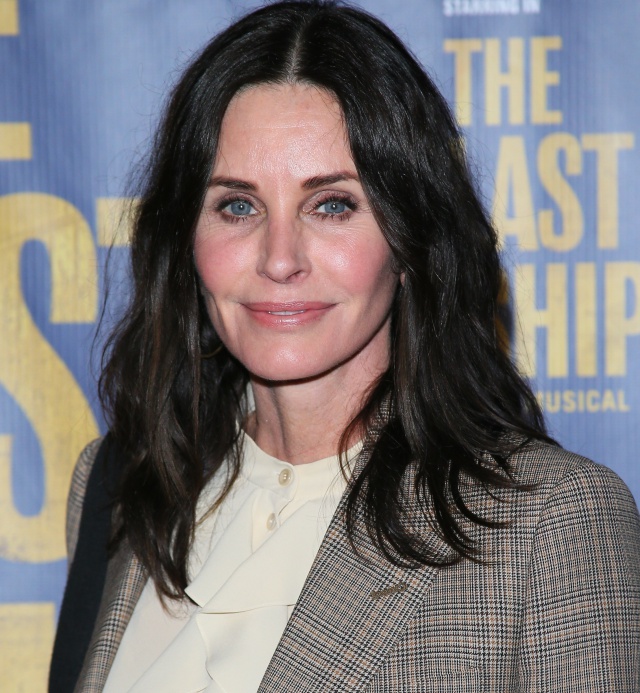 Courtney Cox usando un traje sastre junto a una blusa de color beige mientras posa para la alfombra roja de unos premios