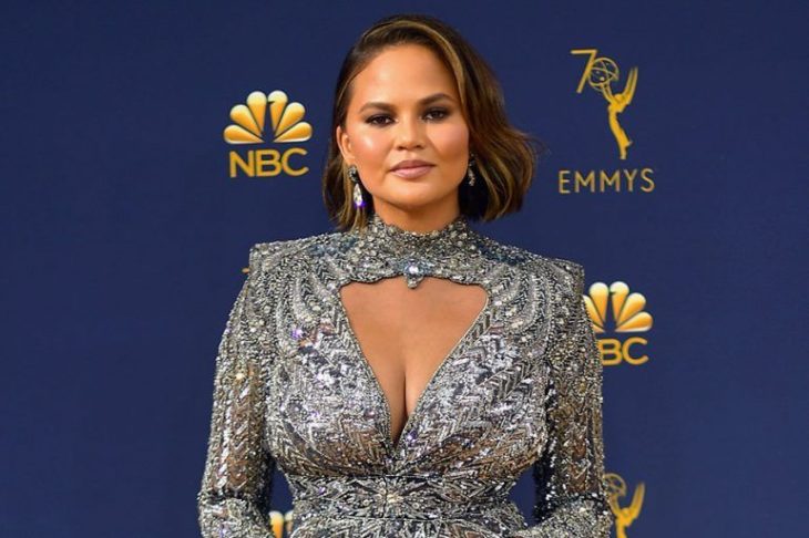 Chrissy Teigen usando un vestido de color plateado con brillos durante la alfombra roja de los EMYS de la cadena NBC