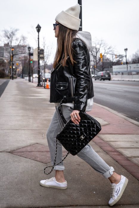 Chica usando chaqueta de cuero negra con pantalón gris, tenis blancos, y gorro blanco
