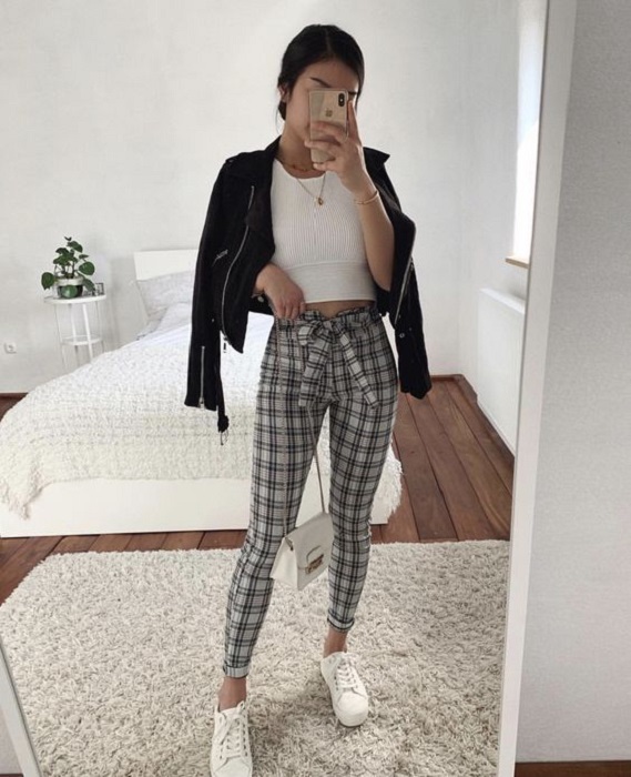 Chica usando chaqueta de cuero negra con pantalón de estampado a cuadros y blusa blanca