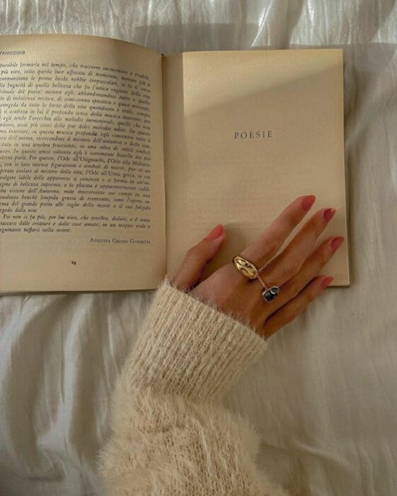 Chica apoyando su manos con las uñas pintadas de rosa sobre un libro con páginas antiguas