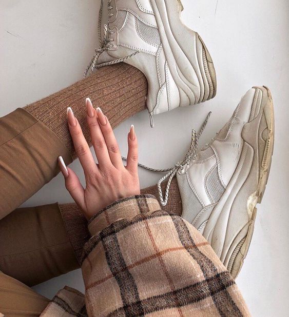 Chica sentada en el piso con outfit café con beige y mano con uñas color beige