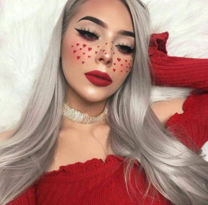 Maquillaje inspirado en San Valentín en colores dorado y guinda, con figuritas de corazón sobre las mejillas