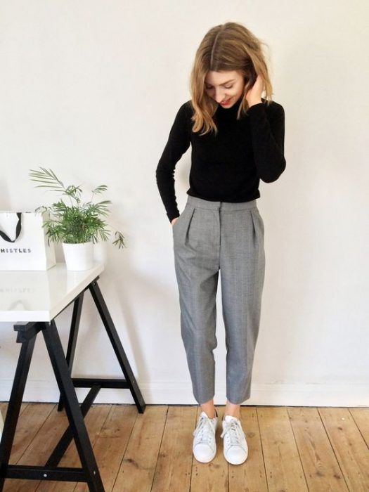 Chica con blusa de manga larga negra, pantalón recto gris, y tenis blancos