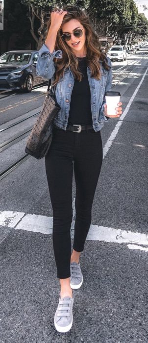 Chica usando leggings y blusa negros, chaqueta denim y tenis grises