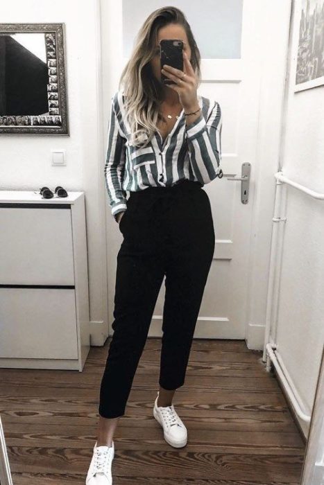 Chica usando una camisa de rayas blancas y verdes, pantalones rectos negros y tenis blancos