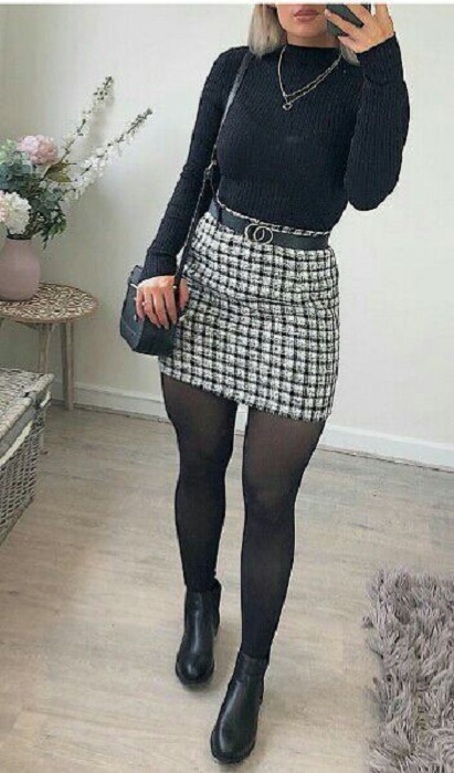 Chica con medias, botines y blusa de manga larga y cuello alto negra con falda de estampado tartán blanco y negro