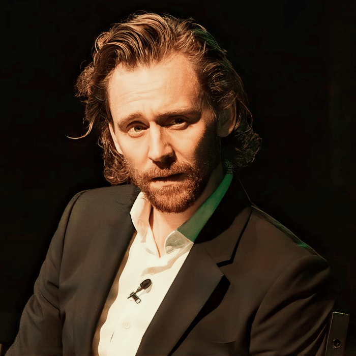 tom hiddleston con cabello largo, barba, camisa blanca y saco negro
