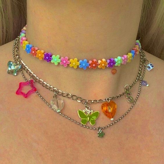 Cuello de una chica rubia usando collares de flores de plástico pequeñas y cadenitas con colgantes en forma de mariposa y corazones