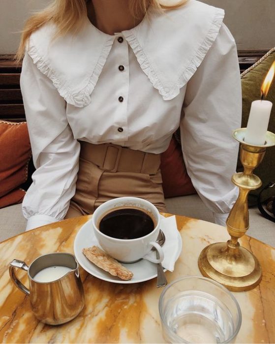 Chica con pantalón café y blusa blanca con cuello bobo
