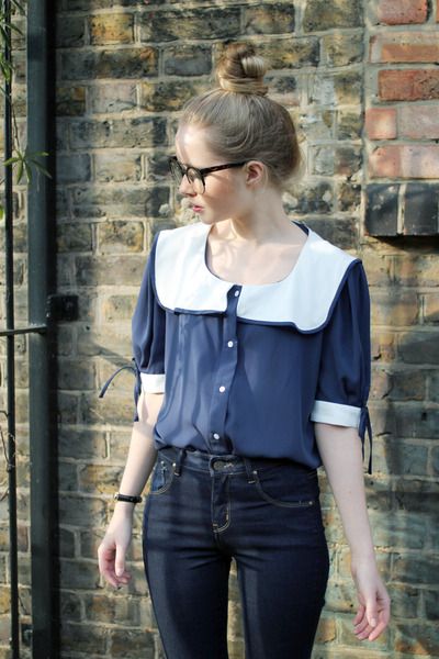 Chica rubia con chongo y lentes con pantalón de mezclilla y blusa azul con cuello bobo blanco