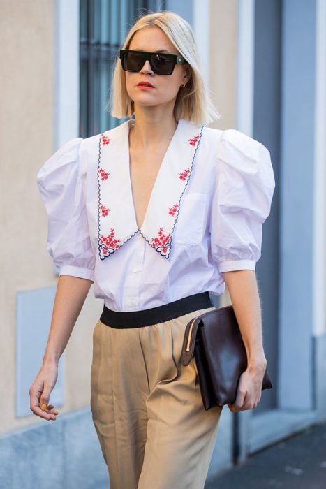 Chica rubia caminando por la calle con pantalón beige y blusa azul claro con cuello bobo