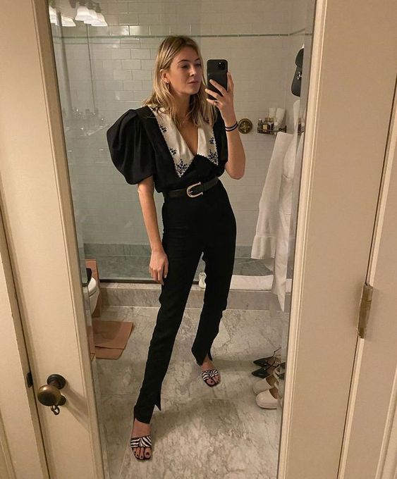 Chica rubia tomando una selfie frente al espejo con blusa negra y cuello bobo blanco y pantalón negro