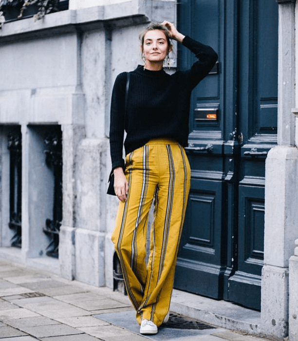 chica de cabello castaño usando un suéter negro con pantalón amarillo de rayas azules con blanco