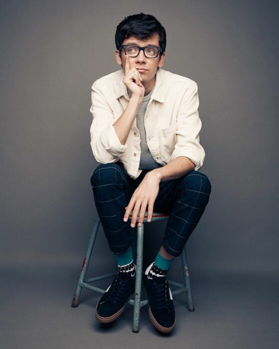 Asa Butterfield sentado en un banco de madera, posando para una fotografía