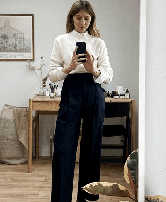 chica rubia usando suéter blanco, camisa blanca debajo, pantalones de vestir azules a la cintura