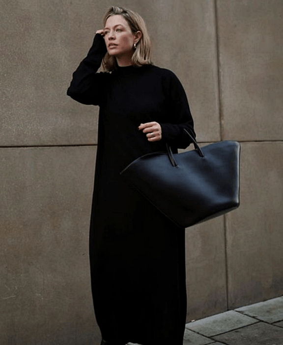 chica rubia usando un vestido tejido negro de manga larga, bolso grande negro de mano