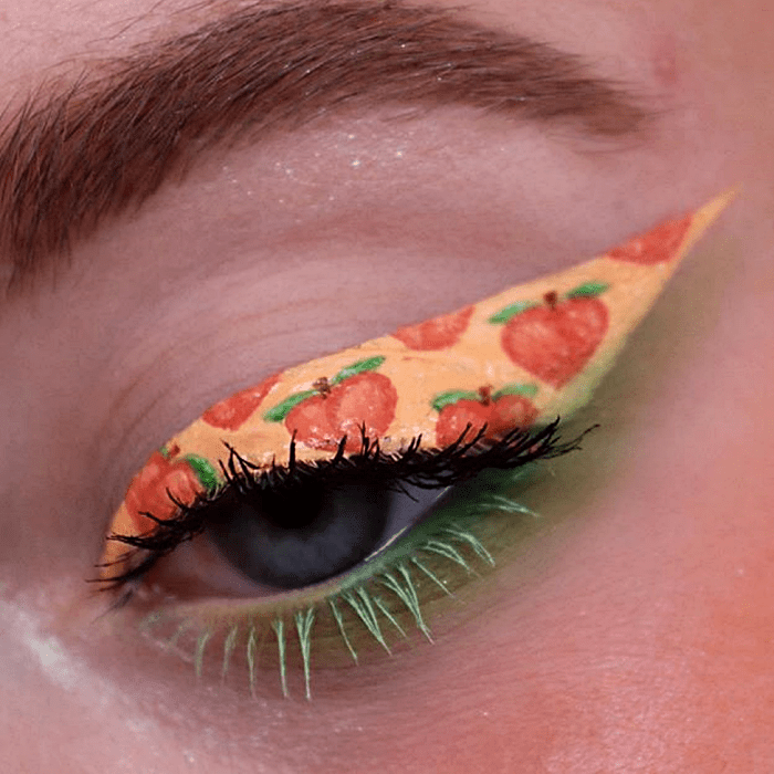 maquillaje de ojos con delineado color naranja claro con dibujos de emoji de durazno y delineado verde y rímel negro y verde