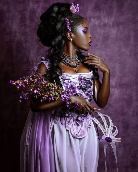 Mujer negra con vestido lila y detalles morados sosteniendo un ramo de flores moradas