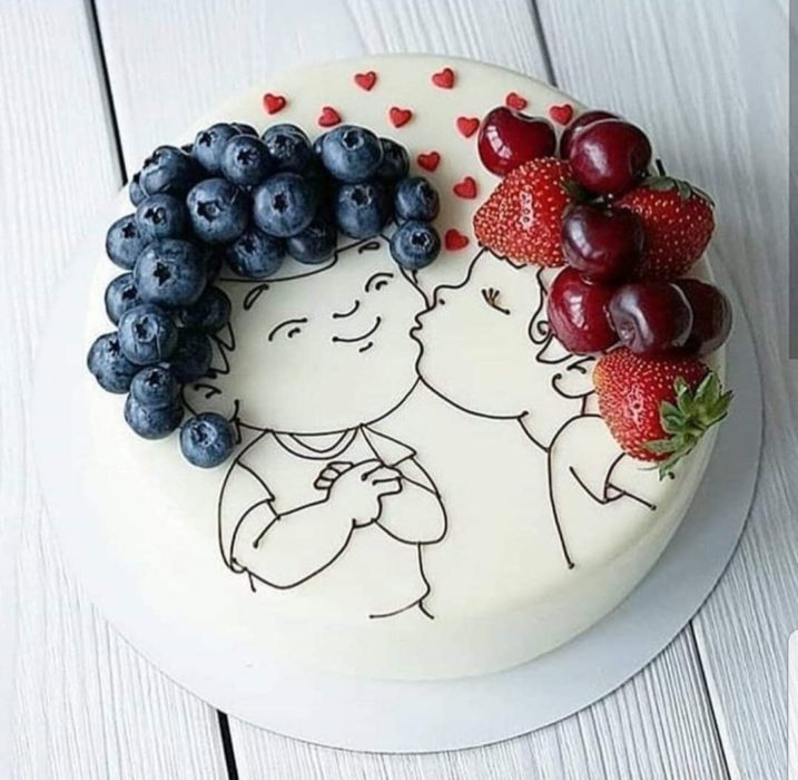 Pastel con cobertura blanca decorado con la silueta de niños con cabello rizado formado con fresas y uvas