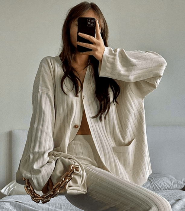 chica de cabello claro usando una camisa oversized blanca beige tejida, pantalones de vestir tejidos beige y bolso de mano beige con cadena dorada