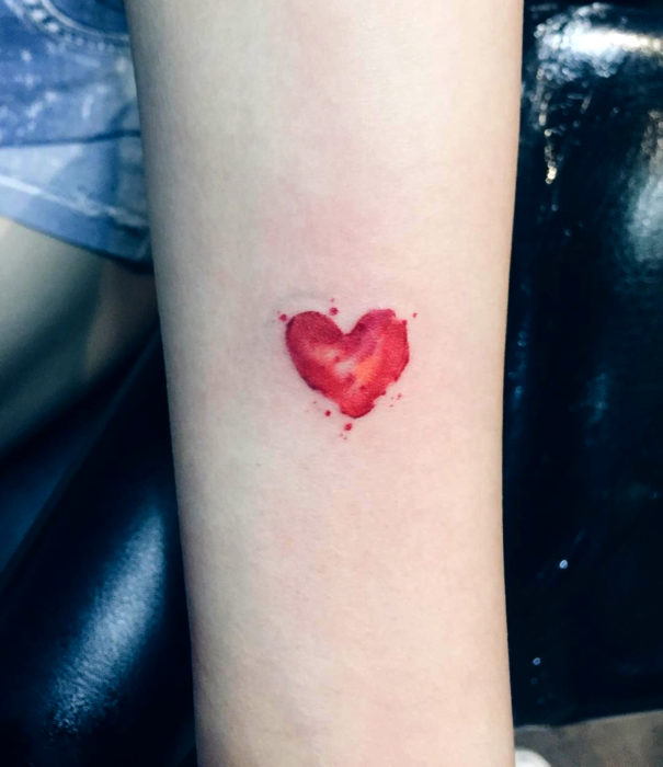 Diseños bonitos de tatuajes de acuarelas; tatuaje de un pequeño corazón rojo en el brazo