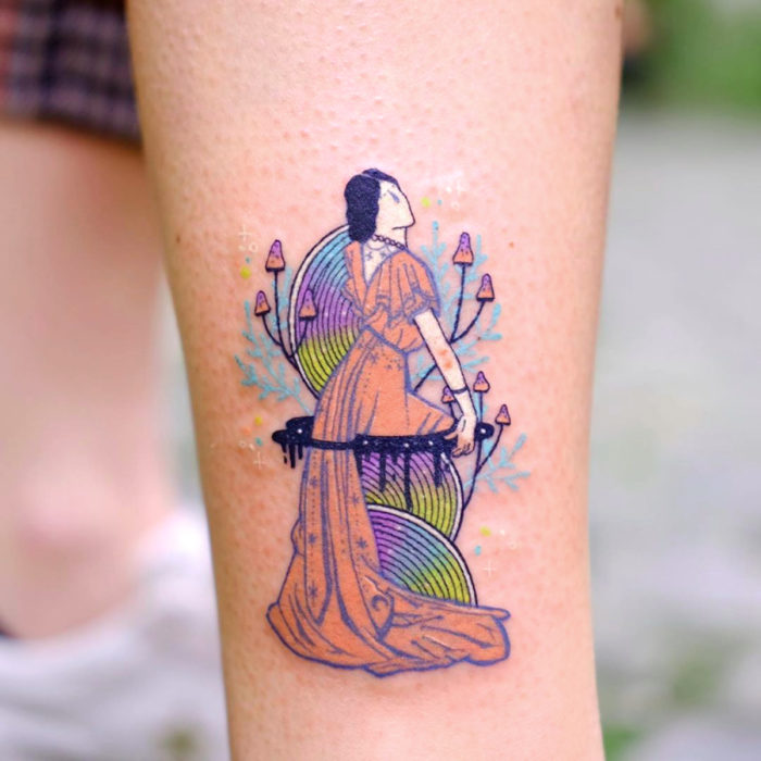 Tatuadora hace tatuajes refinados; tatuaje de mujer con flores y hongos en vestido en el brazo