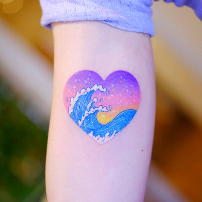 Tatuadora elabora tatuajes artísticos; tatuaje de ola japonesa en un corazón en el brazo